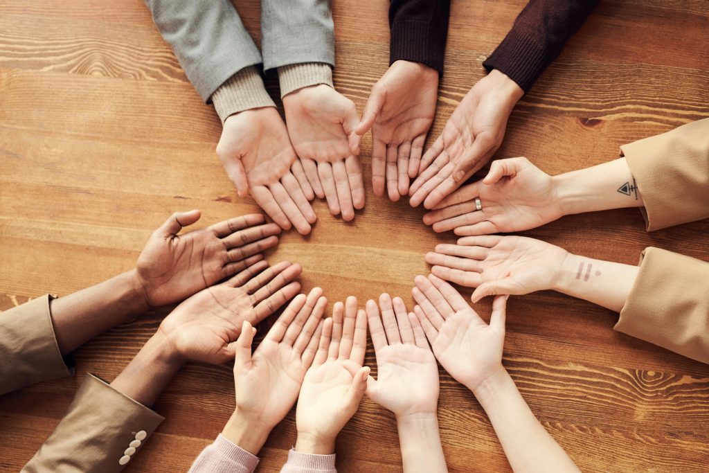 pexels-photo-3184397-3184397 Top view of diverse hands forming a circle on a wooden table, symbolizing unity and diversity.